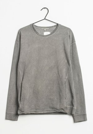 Szara bluza z długim rękawem i okrągłym dekoltem, z kieszeniami bocznymi na szwach, lekko sprana tkanina, zawieszona na czarnym wieszaku na białym tle.