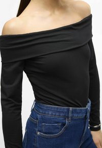 Mustat olkaimeton pitkähihaiset puserot, jotka on yhdistetty korkeavyötäröisiin sinisiin farkkuihin. Sujuva kangas, sopiva siluetti ja hillitty ompelu.