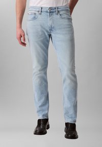 Gaiši zili džinsu džinsi ar taisnu piegriezumu, piecu kabatu dizainu un smalku izbalējumu, kombinēti ar melniem ādas apaviem.