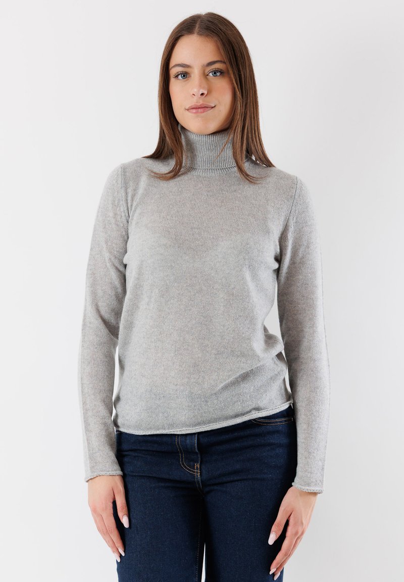 Maglione grigio a collo alto realizzato in un morbido tessuto texturizzato; maniche lunghe e design aderente. Indossato con jeans blu scuro.