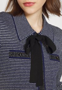 Takit sininen ja valkoinen kuviollinen, jossa on musta solmio kauluksessa, sisältäen kaksi päällystaskua mustilla napilla. Teksturoitu kangas.