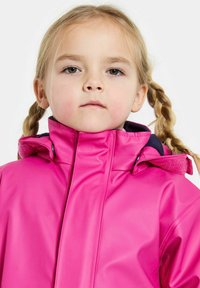 Vaaleanpunainen vedenpitävä takki, jossa on korkea kaulus, teksturoitu kangas ja säädettävä huppu. Takissa on edessä vetoketju ja kontrastivärinen vuori.