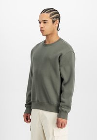 Felpa verde khaki in tessuto morbido, con scollatura a girocollo, polsini a coste e vestibilità comoda. Abbinata a pantaloni cargo chiari.