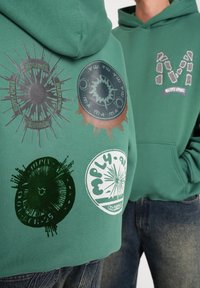 Grøn sweatshirts med forskellige runde grafiske prints i kontrasterende farver og teksturer, med hætte og kængurulomme design.