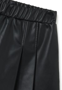 Jupe plissée en simili cuir noir avec une taille élastique. Texture lisse, lignes épurées et design minimaliste. Pas de matériel visible.