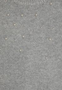 Suéter de punto gris con una tela texturizada y perlas decorativas de diferentes tamaños esparcidas por toda la superficie.