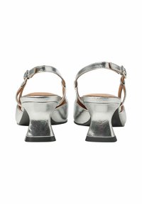 Srebrne metaliczne sandały na obcasie z blokowym obcasem, regulowanym paskiem wokół kostki i gładką teksturą. Otwarty tył i zaokrąglony czubek.
