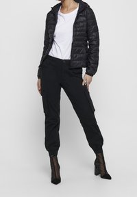 Black puffer jacket with a hood, white t-shirt, and black cargo pants with side pockets. Black ankle boots with mesh detail.