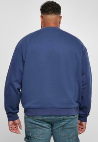 Sudadera azul con cuello redondo, mangas largas y puños acanalados. La tela parece suave y lisa, diseñada para un ajuste relajado.