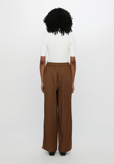 Brown wide-leg trousers with a textured fabric and elastic waistband, paired with a fitted white short-sleeve top.
