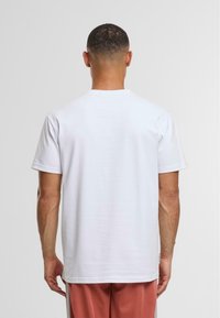 Biała bawełniana koszulka z krótkim rękawem, okrągłym dekoltem i gładkim tyłem, zestawiona z jasnoróżowymi spodniami. Gładka tekstura, casualowy design.
