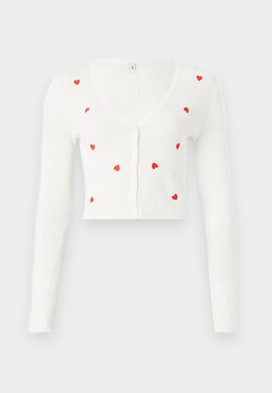 Cardigan blanc côtelé à manches longues, avec des motifs de cœurs rouges. Col en V et fermeture à boutons à l'avant. Longueur cropped.