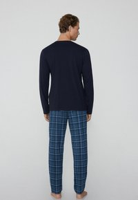 Camisa de manga larga azul marino con pantalones de pijama de cuadros azules, ambos de una tela suave. Los pantalones tienen una cinturilla elástica y un corte holgado.