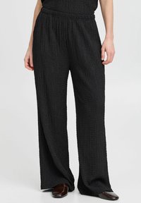 Schwarze, strukturierte weit geschnittene Hose mit einem elastischen Bund. Der Stoff hat eine zerknitterte Optik. Die Hose fällt locker für ein angenehmes Tragegefühl.