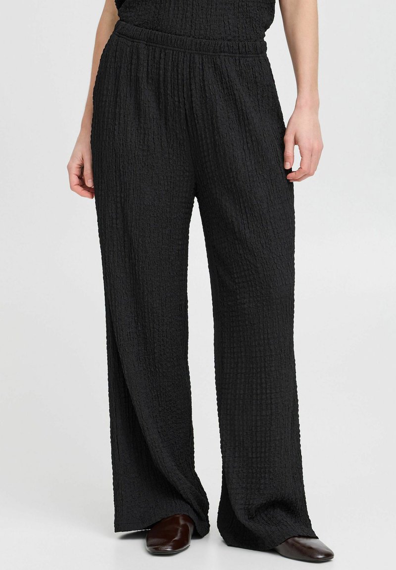 Schwarze, strukturierte weit geschnittene Hose mit einem elastischen Bund. Der Stoff hat eine zerknitterte Optik. Die Hose fällt locker für ein angenehmes Tragegefühl.