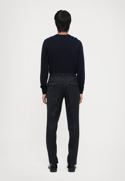 Navy knit sweater and dark trousers with a relaxed fit, featuring a stretchy waistband and two back pockets. Companion shoes black.