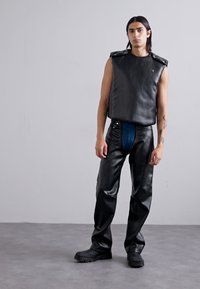 Black faux leather sleeveless top with shoulder accents, paired with black faux leather pants featuring a blue denim front panel. Black chunky footwear.