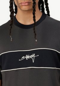 Short-sleeve, dark grey t-shirt featuring a black horizontal stripe with white trim and embroidered "Billabong" logo in the center.