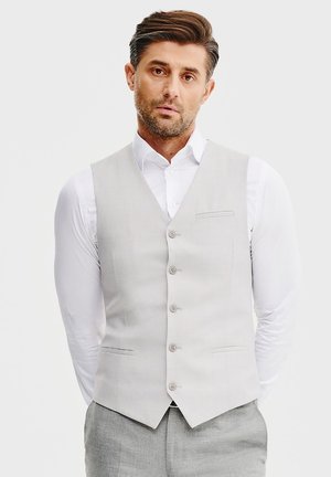 Jasnoszara kamizelka z gładkiego materiału, zapinana na pięć guzików, z jedną kieszonką na piersi. Noszona na białej koszuli, z dopasowanym krojem.