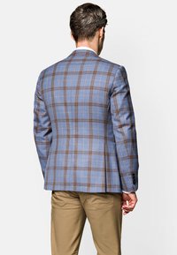 Jasnoniebieska marynarka w kratę z brązowymi i białymi liniami, z pojedynczym rozporkiem z tyłu i czarnymi guzikami na mankietach. Spodnie są w kolorze khaki.