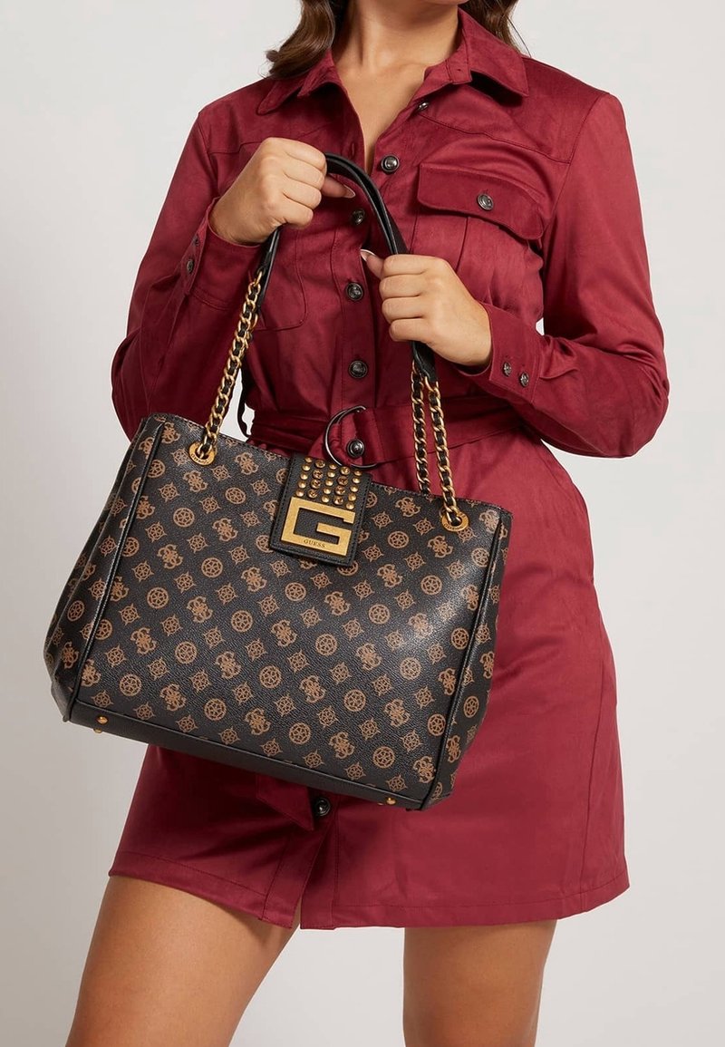 Femme portant une robe rouge boutonnée tenant un sac à main noir et marron à motifs avec des anses en chaîne dorée et un fermoir décoratif.