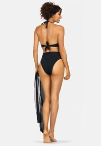 Czarny strój kąpielowy w paski z halterem i zawiązywaniem z tyłu. Wysokie majtki. Lekka czarna narzutka opadająca na bok. Gładka tekstura.