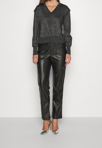 Schwarzer glitzernder V-Ausschnitt-Pullover mit langen Ärmeln, kombiniert mit schwarzen Lederhosen mit Reißverschlusstaschen und silbernen High-Heels.