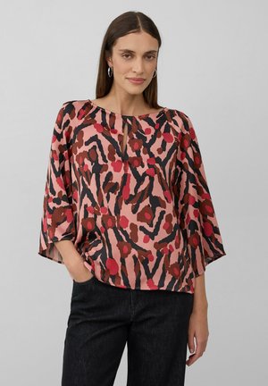 Blouse fluide rose avec un motif abstrait noir et rouge, dotée d'un col en keyhole et de manches larges, fabriquée en tissu léger.