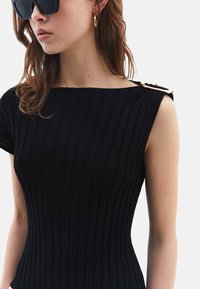 Abito nero a coste con scollatura ampia, maniche corte e un accento dorato sulla spalla. Tessuto liscio, silhouette aderente.