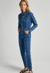 Džínový overal v vybledlé modré barvě, s límečkem, předním zapínáním na knoflíky a dvěma náprsními kapsami. Úzký střih se rovnými nohavicemi, délka po kotníky a jemné švy.