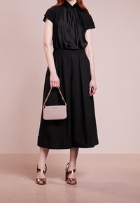 Czarna satynowa bluzka z rękawami typu cap, wysokim dekoltem i luźnym krojem. Szerokie czarne spodnie z mankietami na końcach nogawek. Złote sandały na wysokim obcasie z paskami oraz mała różowa torebka.