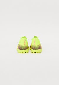 Neon gule sportssko med en tekstureret overdel med multikolorede vandrette striber, gummisåler med mønster, og et logo på bagsiden.