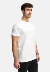 Weißes Baumwoll-T-Shirt mit kurzen Ärmeln, rundem Ausschnitt und lockerer Passform. Glatte Textur, keine sichtbaren Muster oder Grafiken.