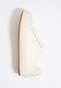 Canvas sneaker in cream with a textured upper, round toe, five metal eyelets, and a rubber gum sole. Side stitching detail visible.