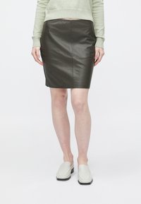 Rjava usnjena krilo za svinčnik z gladko teksturo in oprijeto zasnovo, kombinirana z svetlo zelenim puloverjem in belimi čevlji brez zavezovanja.