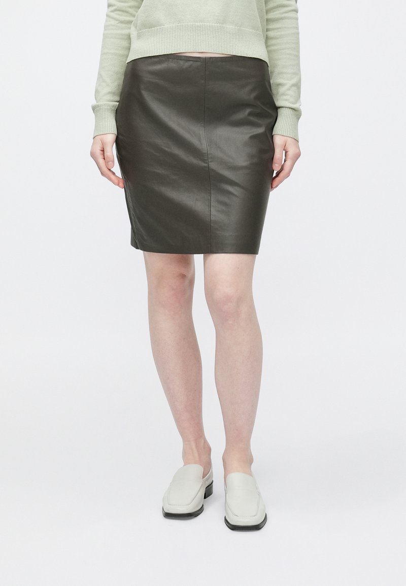 Rjava usnjena krilo za svinčnik z gladko teksturo in oprijeto zasnovo, kombinirana z svetlo zelenim puloverjem in belimi čevlji brez zavezovanja.