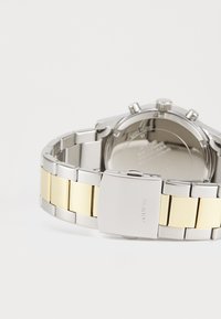 Orologio in acciaio inossidabile argento e oro con bracciale bicolore, chiusura piatta e quadrante rotondo minimalista. Finitura metallica liscia.