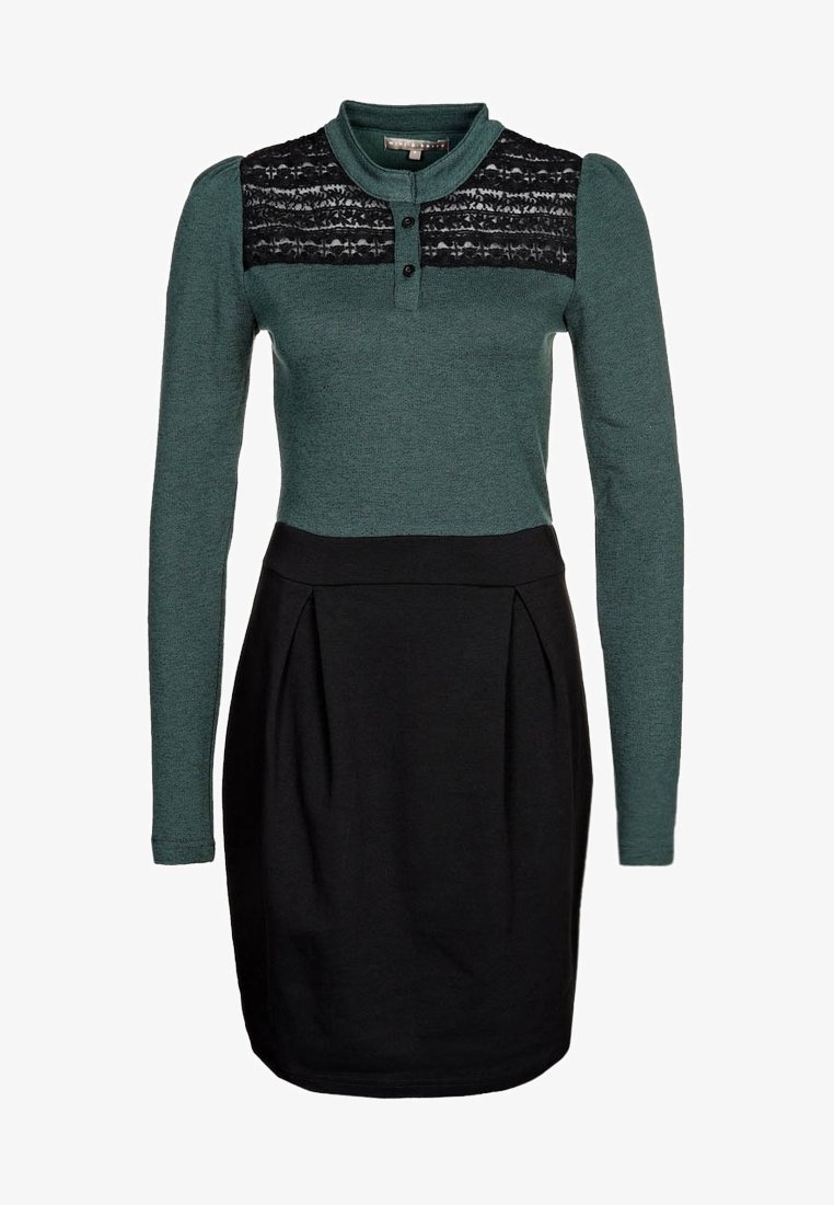 Robe verte à manches longues avec un panneau en dentelle noire aux épaules, corsage ajusté et jupe noire évasée avec des plis.