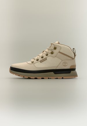 Μπεζ μπότες Timberland ψηλές με μαύρη και καφέ σόλα, μεταλλικά κορδόνια και επένδυση στο κολάρο σε ουδέτερο φόντο.