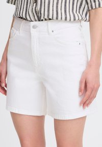 Pantalones cortos de denim blanco con corte recto, que cuentan con un diseño clásico de cinco bolsillos y un botón metálico visible en la cinturilla.
