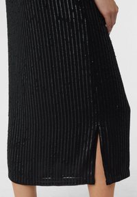 Zwarte jurk met verticale strepen en pailletten. De stof heeft een zachte textuur en is voorzien van een zijsplit voor extra bewegingsvrijheid.