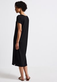 Černé proužkované midi šaty s krátkými rukávy, postranním rozparkem a kulatým výstřihem. Materiál je jemný s výraznou texturou, doplněný o ploché sandály.