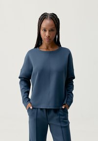 Granatowy sweter z okrągłym dekoltem i opuszczonymi ramionami, o gładkiej teksturze i widocznych detalach szwów, w komplecie z dopasowanymi spodniami.