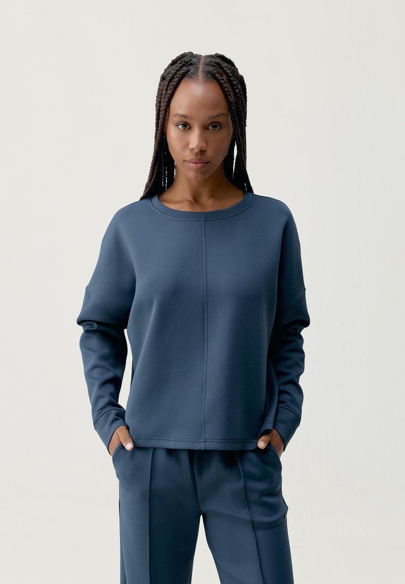 Granatowy sweter z okrągłym dekoltem i opuszczonymi ramionami, o gładkiej teksturze i widocznych detalach szwów, w komplecie z dopasowanymi spodniami.