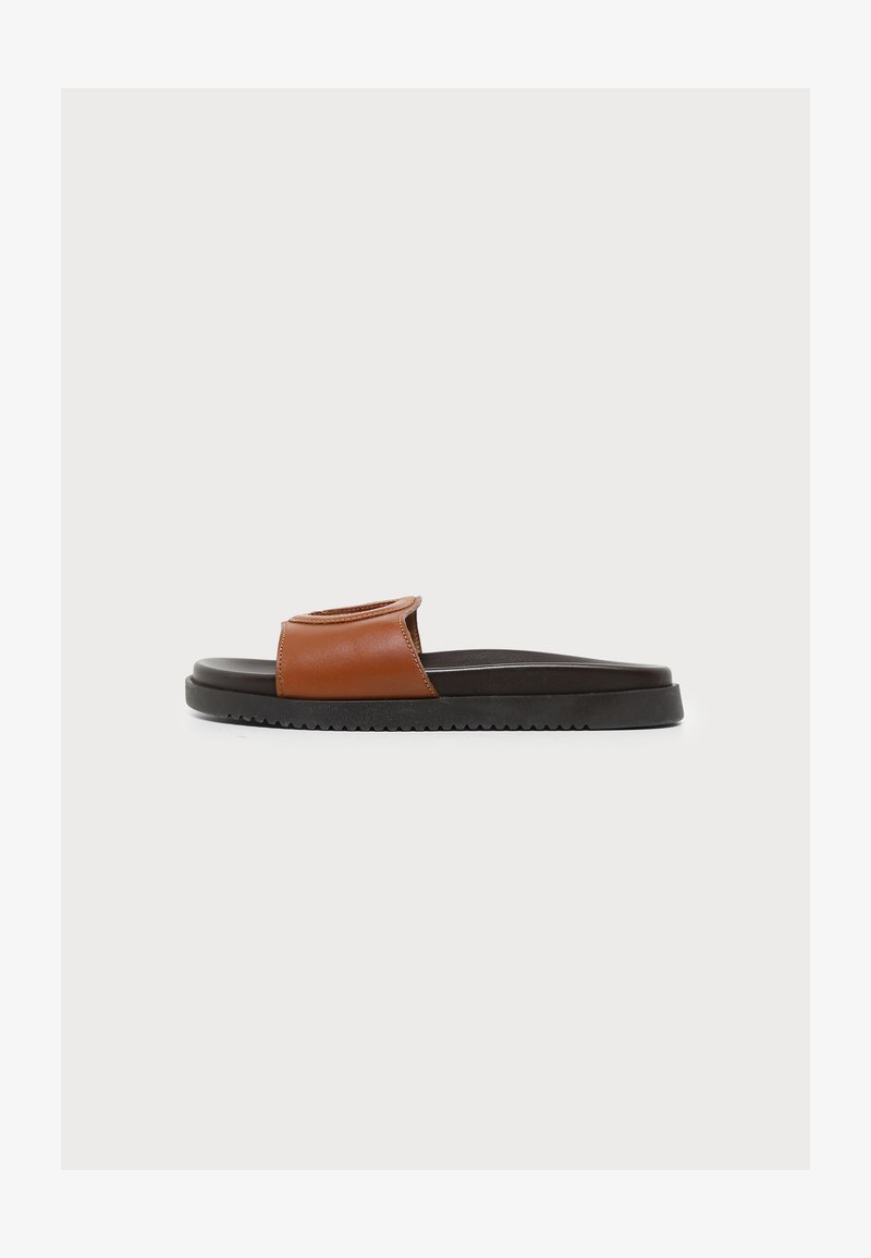 Une sandale mule en cuir marron avec une semelle noire, un talon plat et une large bride sur le dessus, vue de profil sur fond blanc.