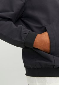 Navy bomber jacket featuring elastic cuffs and waistband, with a smooth, lightweight fabric and side pocket integrated into the design.