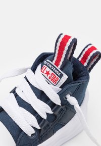 Modré plátěné tenisky s vysokým vzorem, bílé tkaničky, s červenou a bílou pruhovanou patkou a výrazným logem "All Star" na jazyku.