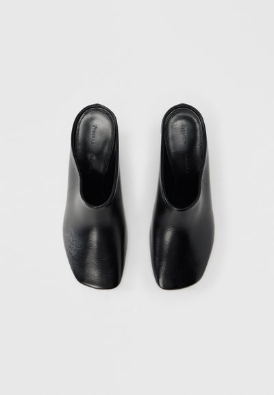 Μαύρα δερμάτινα mules με λεία υφή, ανοιχτή πλάτη και τετράγωνη μύτη. Μινιμαλιστικός σχεδιασμός χωρίς εμφανείς διακοσμήσεις ή μεταλλικά στοιχεία.
