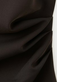 Gros plan sur un tissu marron foncé avec des plis doux et diagonaux créant des plis texturés sur une surface lisse et mate.