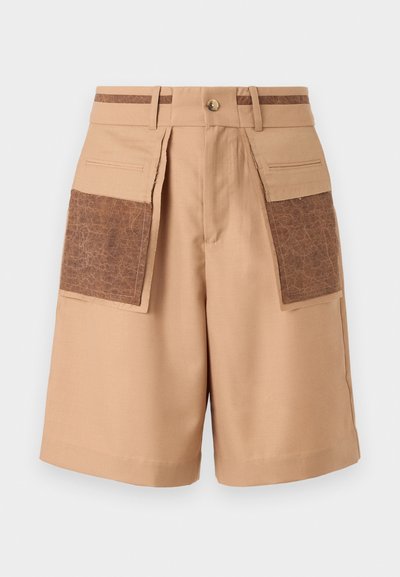 Beige tailored shorts featuring two large brown faux leather pockets, a front button closure, and belt loops with a contrasting stripe.